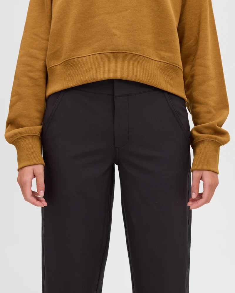 Tentree Breton Pant A person wearing a cropped mustard yellow sweatshirt and black trousers, shown from the chest down against a light gray studio background.