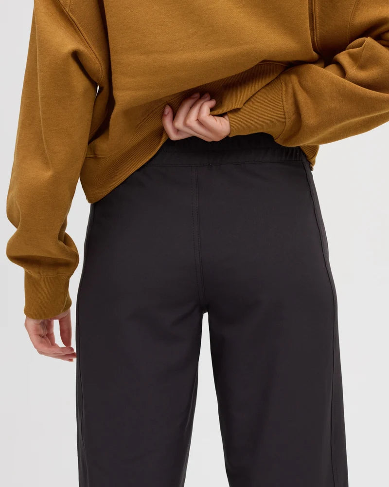 Tentree Breton Pant Close-up of a person wearing black wide-leg sweatpants and a cropped mustard yellow sweatshirt, shown from the back against a light gray studio background.
