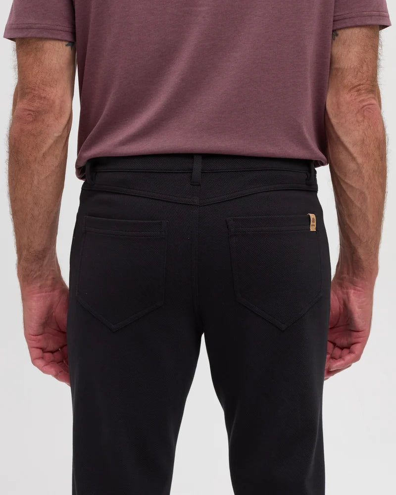 The back view of a man wearing black Clark pants from Tentree and a purple shirt
