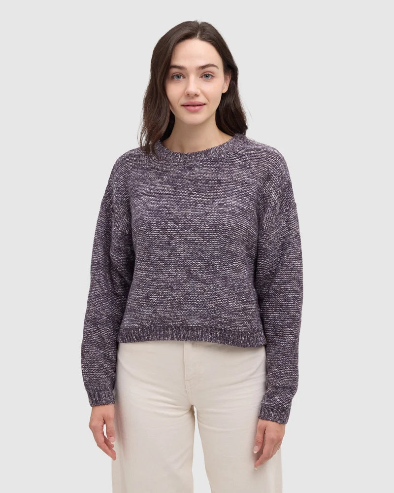 A woman wearing a purple plum sweater and white pants.