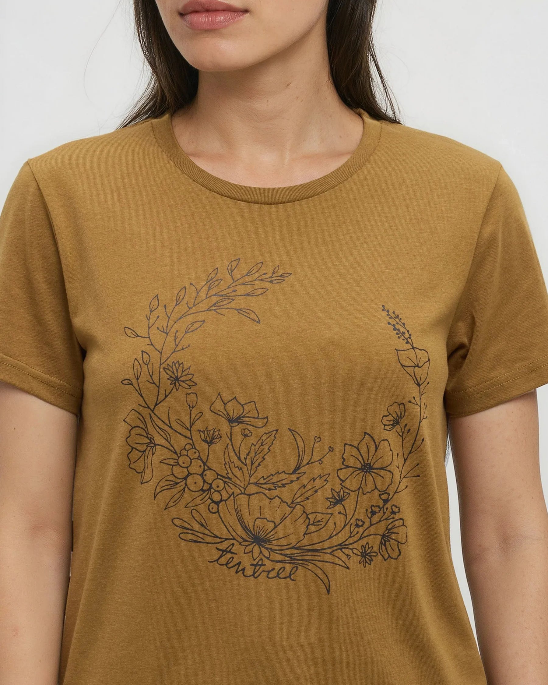 Tentree Evergreen Floral Tee A woman wearing a mustard yellow crewneck t-shirt with a black line art floral wreath graphic on the front.