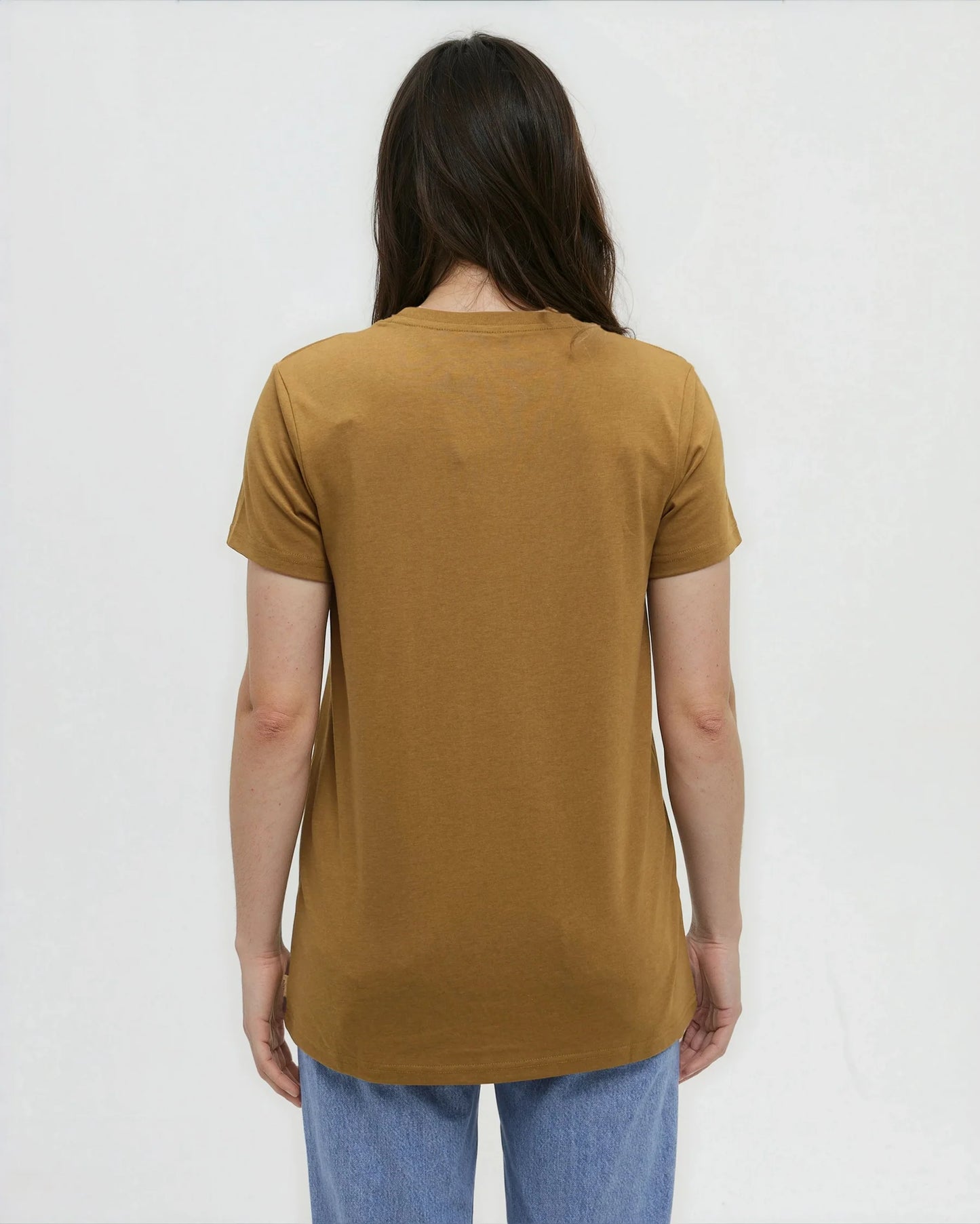 Tentree Evergreen Floral Tee A woman viewed from behind wearing a mustard yellow short-sleeve t-shirt and blue jeans against a plain white background.