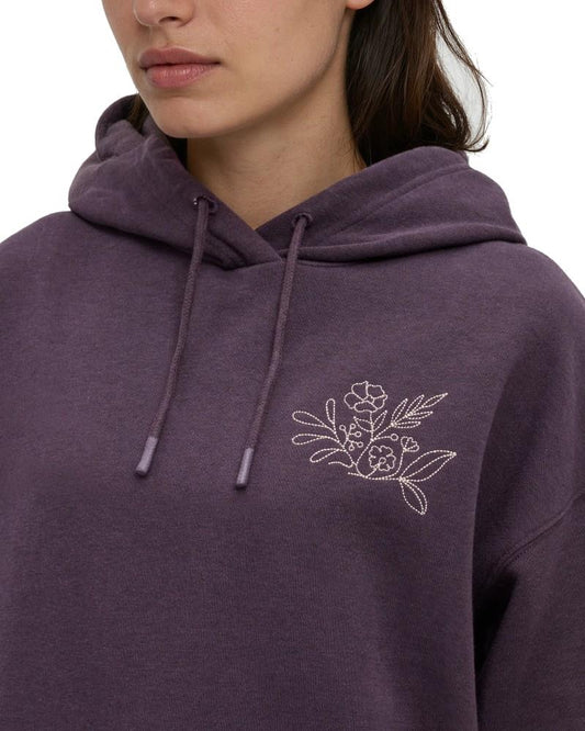 Tentree Field Foliage Hoodie A close-up of a person wearing a heathered purple pullover hoodie with a white embroidered floral design on the left chest and matching drawstrings.