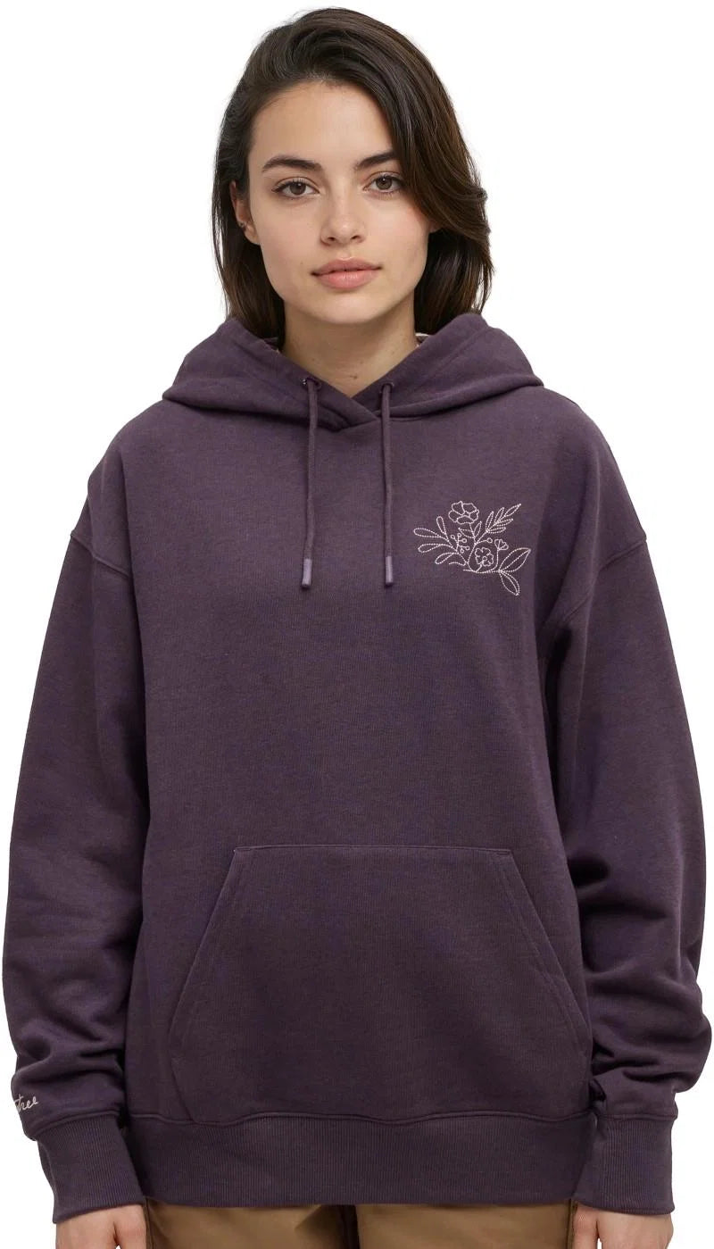 Tentree Field Foliage Hoodie A woman wearing a dark purple pullover hoodie with a small white floral graphic on the left chest, photographed against a plain white background.