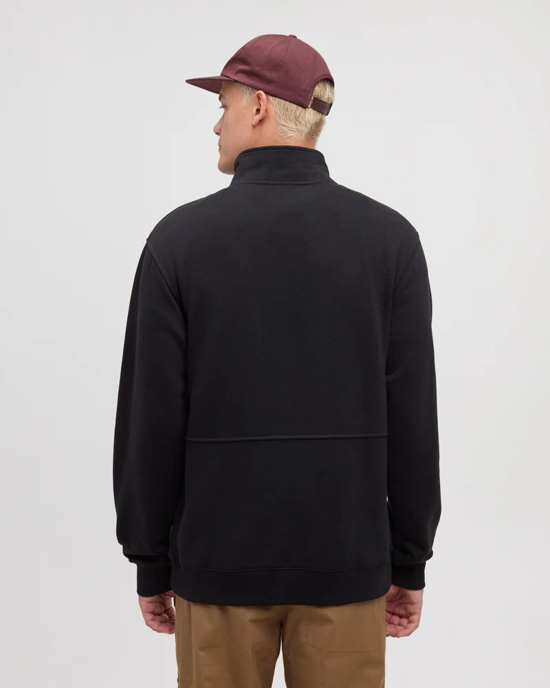 The back view of a man wearing tan pants and a black sweater with a hat on