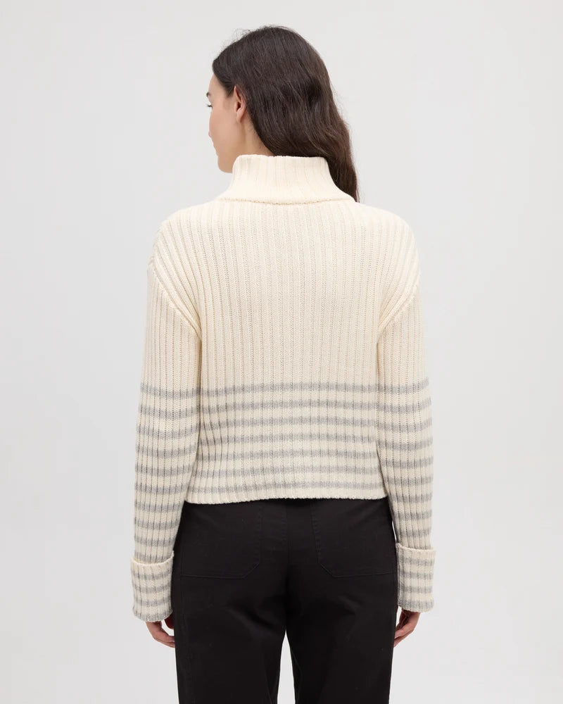 The rear view of a woman wearing black pants and and a cream and grey striped monarch cardigan