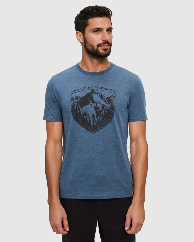 Tentree Protect Tee A man wearing a heather blue crewneck t-shirt with a dark graphic print of a mountain and the text 'PHOENIX ROCK CLIMBING', paired with black pants, against a light gray background.