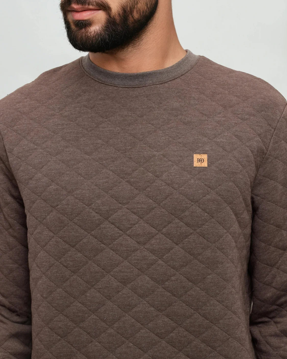 A man wears a quilted sweater in a plain white room