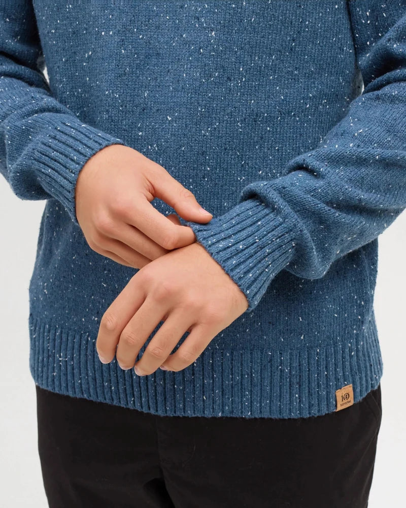 A close up of a man adjusting the hem of his sleeve on is blue fleck rambler sweater
