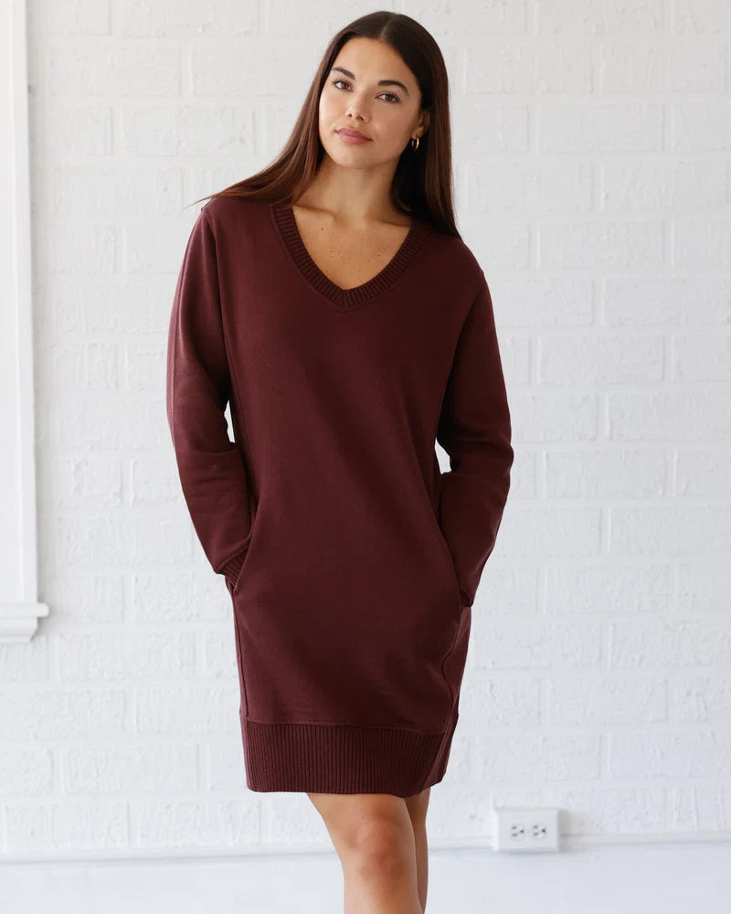A woman stands in industrial room wearing a dress and hands in pockets.