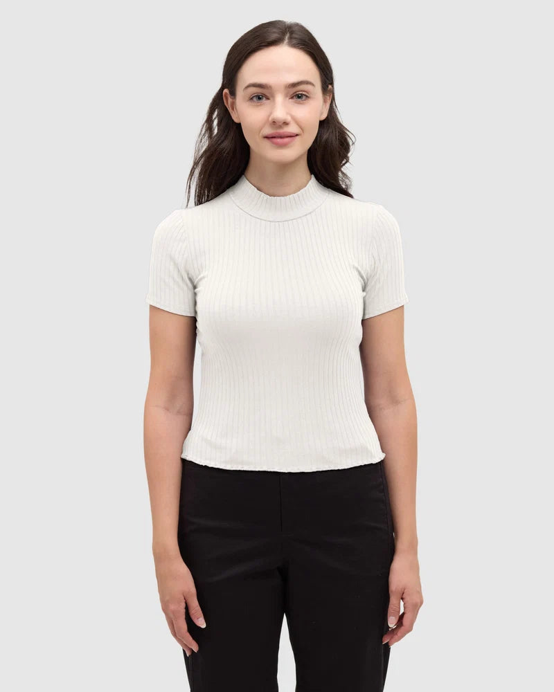 Tentree Whitney Mockneck A woman modeling a short-sleeve ribbed mock neck top in off-white, paired with black pants, against a solid light gray background.