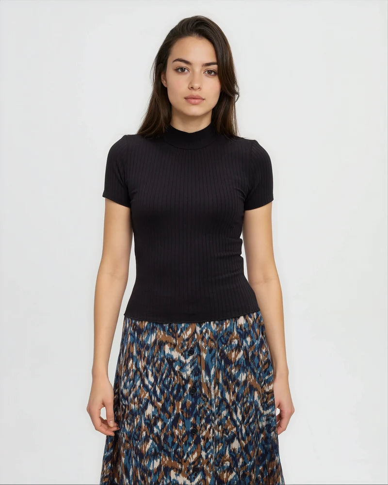 Tentree Whitney Mockneck A woman modeling a black short-sleeve ribbed mock neck top paired with a blue, brown, and white patterned skirt, set against a plain light gray background.
