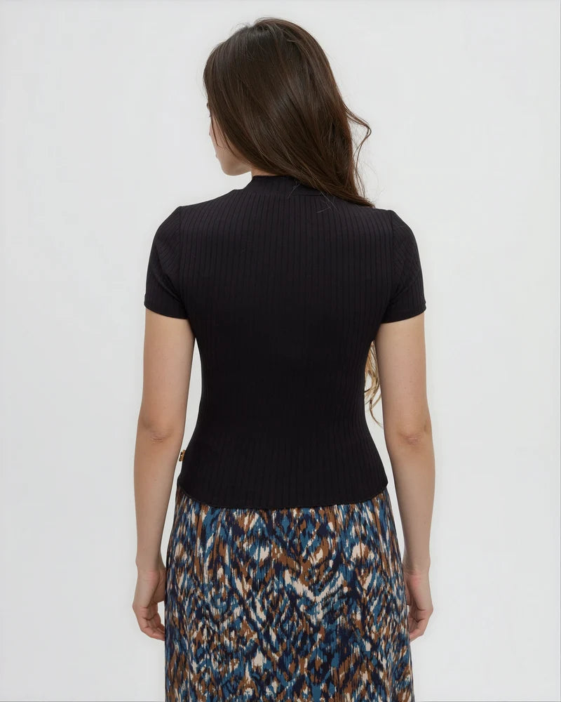 Tentree Whitney Mockneck A woman shown from the back wearing a black ribbed short-sleeve mock neck top and a blue, brown, and cream patterned skirt, against a plain light gray background.