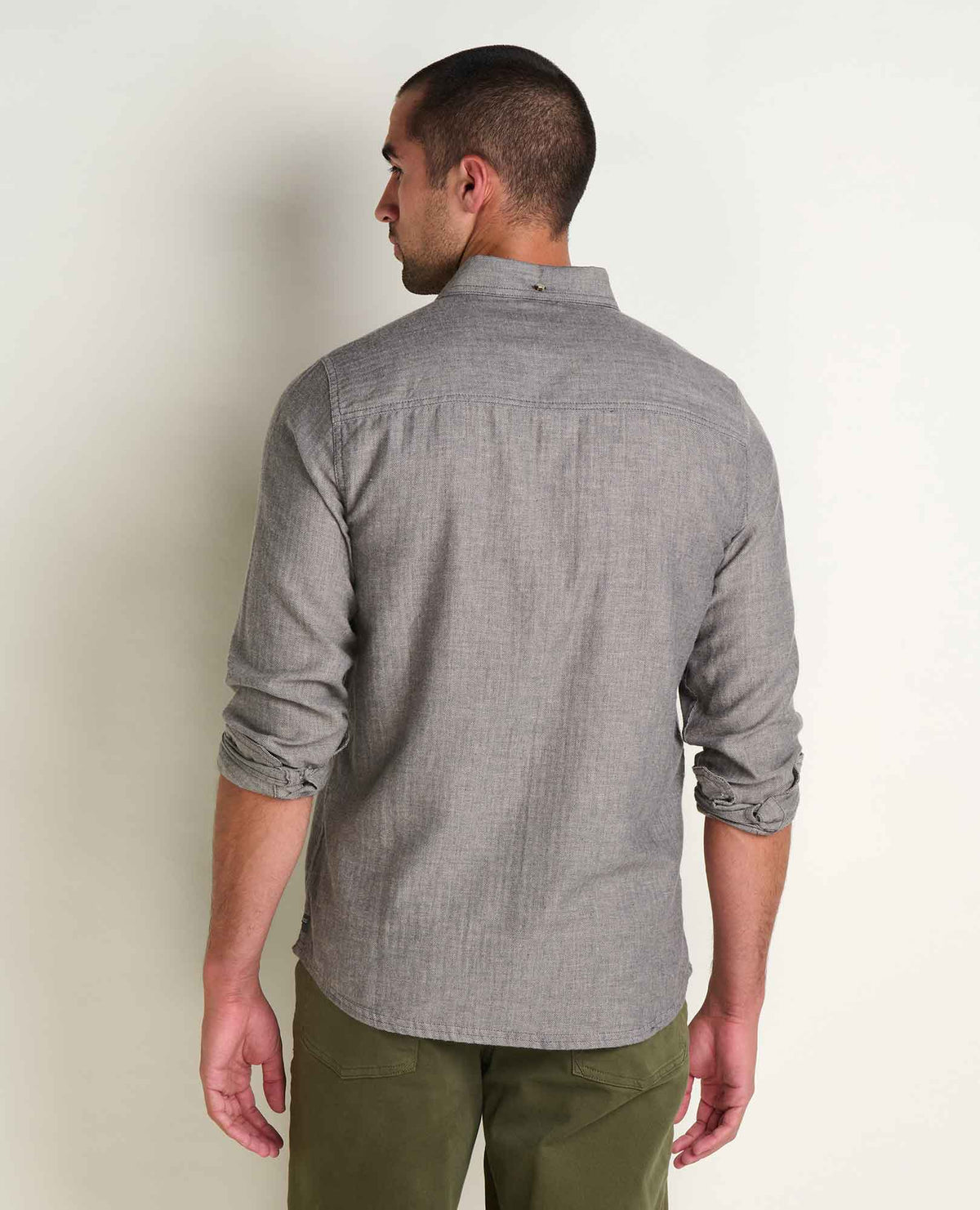 Toad & Co Airsmyth Long Sleeve Shirt A man shown from the back wearing a light gray textured long-sleeve button-down shirt and olive green pants, standing against a plain off-white wall.