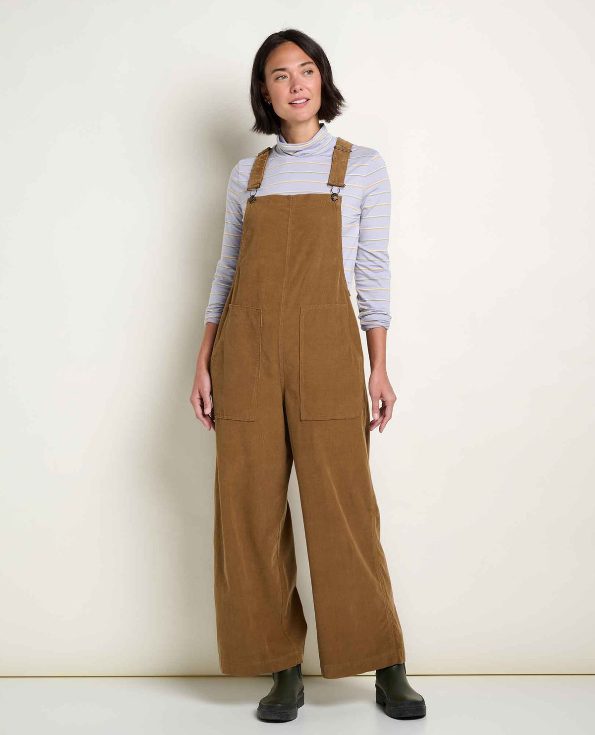Women wears a corduroy overall standing in a studio with off white walls