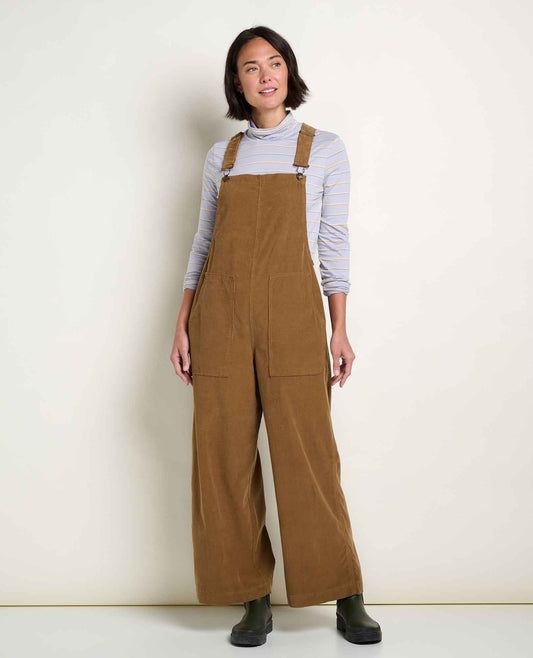 Women wears a corduroy overall standing in a studio with off white walls
