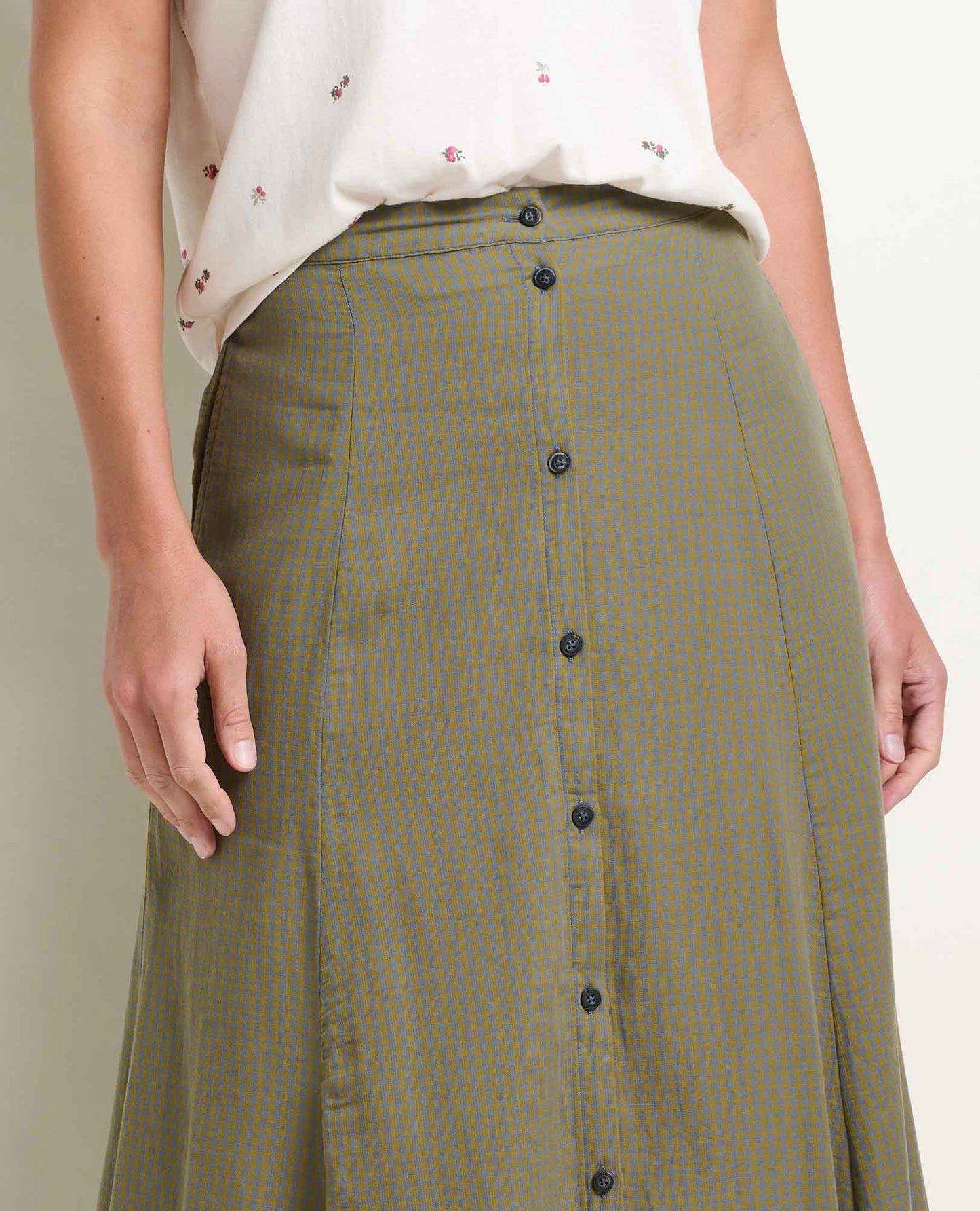 Toad and Co Manzana Organic Cotton Midi Skirt Green Moss Pattern  A close-up of a person wearing an olive green skirt with a fine blue and yellow gingham check pattern, front button closure, and a white sleeveless top with small floral prints.