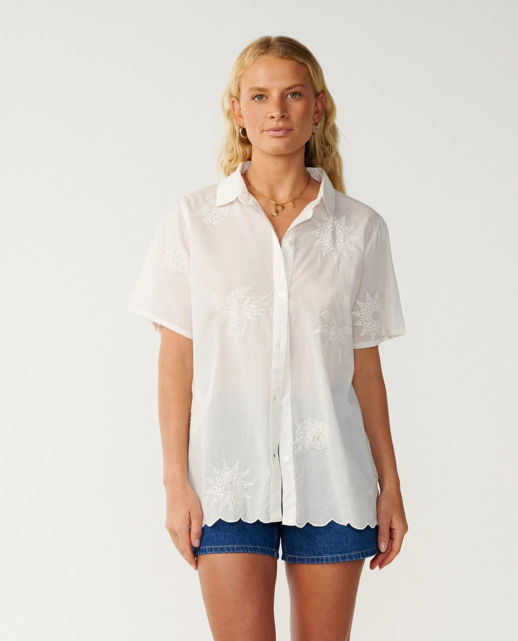 Rip Curl Bossa Nova Emb Short Sleeve Shirt Woman wearing a white blouse with scalloped edges and blue shorts on a plain background