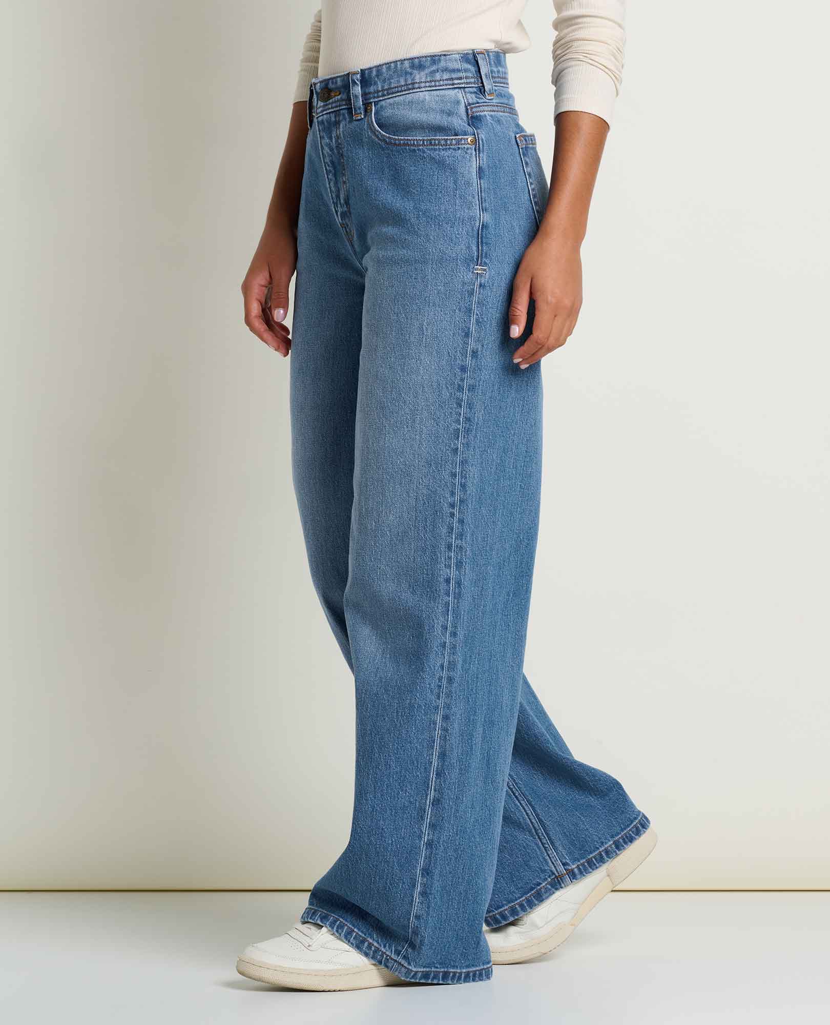 toad and co tamarack wide leg jeans A person wearing high-waisted, wide-leg blue denim jeans with a cream ribbed long-sleeve top and white sneakers, shown from the waist down against a plain off-white studio background.